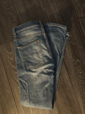 Nudie Jeans ljusblå slim  - Säljer ett par ljusblå jeans från Nudie Jeans med unik wash 🧽  snygg slitning.✅ Jeansen har knappgylf och smal passform som sitter snyggt längs benen. Perfekta för dig som gillar en stilren look.