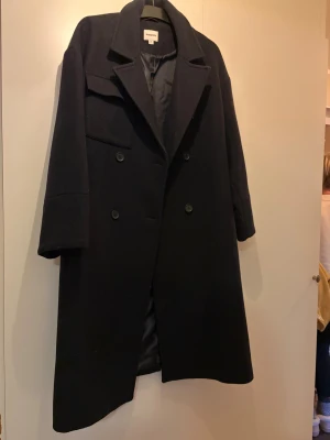 Svart ullkappa från Kappahl, M - Säljer en svart, lång ullkappa från Kappahl i storlek M. Kappan har dubbelknäppning med stora knappar, klassisk krage och en ficka med lock på bröstet. Perfekt oversized look och tidlös design som funkar till allt.