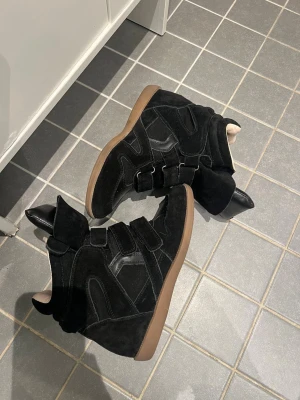 Svarta Isabel Marant sneakers med kilklack - Säljer min flickväns svarta sneakers från Isabel Marant med kilklack och platt gummisula. Skorna har mocka och skinnpaneler, samt tre breda kardborreband över foten. Insidan är ljusbeige och tungan är extra vadderad för en cool look💕! Tar gärna emot frågor det är bara att skriva om ni undrar något☺️