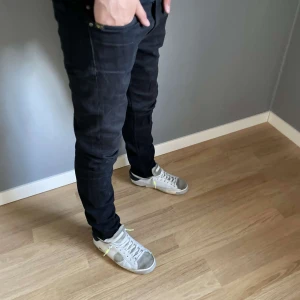 Nudie jeans - Säljer ett par svarta jeansbyxor med slim passform. Klassisk femficksmodell och normal midja. Jeansen har raka ben och är tillverkade i ett stretchigt material för extra komfort. Perfekta för en stilren och enkel look. Kille som står där är 170cm och väger ca 55-60kg.pris är inte hugget i sten pga liten defekt i under delen