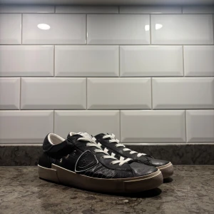 Svarta sneakers från Philippe Model - Svarta sneakers från Philippe Model med vit sula och vita snören. Skorna har en rund tå, detaljerade sömmar och metallnitar på sidan. Tillverkade i skinn med vita insidor och kantdetaljer. Snygg look som passar till jeans. Pris går att förhandlas vid snabb affär👍
