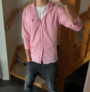 Rosa skjorta från Ralph Lauren - Snygg rosa skjorta från Ralph Lauren med klassisk krage och knappar framtill. Skjortan har lång ärm och den ikoniska broderade loggan på bröstet. Perfekt för dig som gillar stilrena och färgglada plagg. Materialet känns lätt och skönt mot huden.