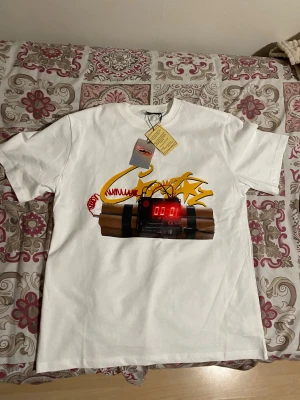 Cortiez t-shirt - Säljer en vit t-shirt med ett stort grafiskt tryck på framsidan som föreställer en digital timer och dynamit, samt graffiti-inspirerade detaljer i gult och rött. På baksidan står det 'TIMES UP BITCH' i fet svart text. Klassisk rund hals och korta ärmar.