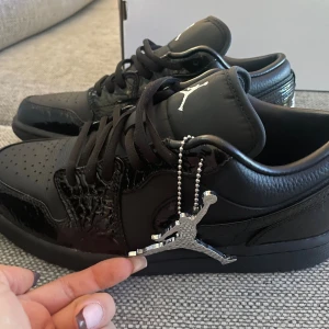 Nike Air Jordan 1 Black - Säljer ett par Nike Air Jordan 1 Low i helsvart färg. Skorna har en mix av matt och glansig läderfinish med snygga detaljer och klassisk Jumpman-logga. Låga sneakers med snörning, perfekta för dig som gillar stilrena och sportiga vibes. Passar både tjejer och killar beroende på vilken strl du brukar ha☺️Väldigt rimligt pris med tanke på kartongen och alla tillbehör när tidigare pris kostade dubbelt så mycket. Storleken var för liten för mig och hade tyvärr råkat dra bort taggen som man kan se.