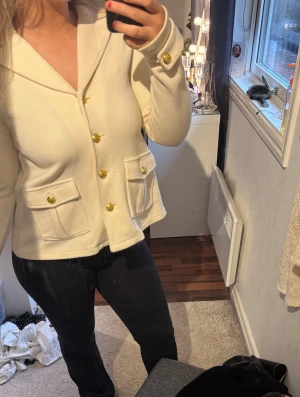 Beige kofta med guldknappar - Snygg beige kofta med guldiga knappar och två fickor framtill. Koftan har en krage och långa ärmar med dekorativa knappar vid ärmslut. Materialet känns mjukt och har en lätt struktur, perfekt för att lyfta din outfit.kan användas som både jacka eller tröja.Vid snabb affär kan priset diskuteras. Har du frågor, bara att skriva💞