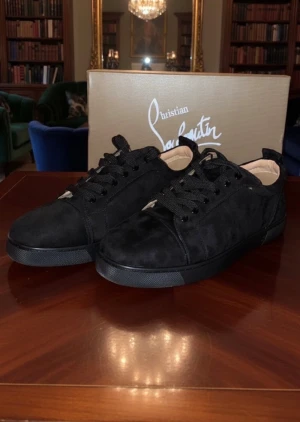 Christian Louboutin svarta sneakers mocka - Svarta sneakers från Christian Louboutin i mjuk mocka med klassisk snörning och rund tå. Insidan är beige och yttersulan har den ikoniska röda färgen med Louboutin-logga. Snygg och stilren design som sticker ut med exklusiva detaljer.