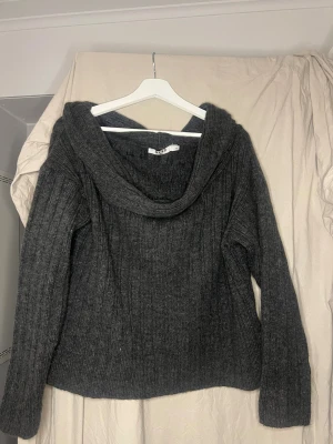 Mörkgrå stickad off-shoulder från NA-KD - Mysig mörkgrå stickad off-shoulder från NA-KD i storlek M. Tröjan har ribbad struktur som ger en cool vibe. Perfekt för kyliga dagar och enkel att styla med jeans eller kjol. Långärmad och loose fit för extra komfort.