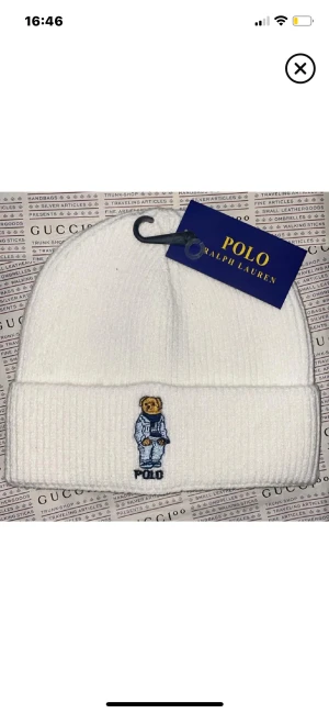 Vit ribbad mössa Polo Ralph Lauren - Vit ribbad mössa från Polo Ralph Lauren med broderad ikonisk björn på uppviket. Klassisk och clean design, perfekt för att hålla värmen och samtidigt se fresh ut. Materialet är mjukt och stickat för extra komfort.