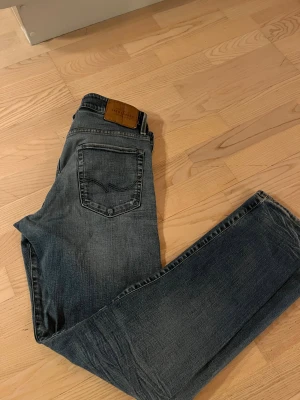Blå jeans från Jack & Jones - Säljer ett par blå jeans från Jack & Jones med snyggt slitna detaljer och klassisk femficksdesign. Jeansen har rak passform. 