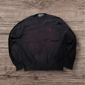 Mörkblå v-ringad tröja från Polo Ralph Lauren - Mörkblå v-ringad tröja från Polo Ralph Lauren i storlek L. Tröjan är tillverkad av mjuk pima bomull och har ett rött broderat Polo-logo på bröstet. Klassisk passform med långa ärmar och ribbade muddar vid ärmslut och nederkant.