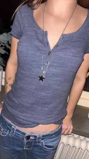 Blå ribbad topp med knappar - Säljer en blå ribbad topp med korta ärmar och u-ringning med fem knappar framtill. Toppen har en slim passform och är tillverkad i mjukt bomullsmaterial. Perfekt att styla med jeans för en chill look.