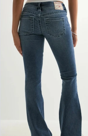 True Religion bootcut jeans blå - Säljer ett par klassiska blå jeans från True Religion med ikoniska bakfickor och snygg bootcut-passform. Jeansen har normal midja, fem fickor och tydliga kontrastsömmar. Perfekta för dig som gillar en tidlös och avslappnad stil. Knappt använda.