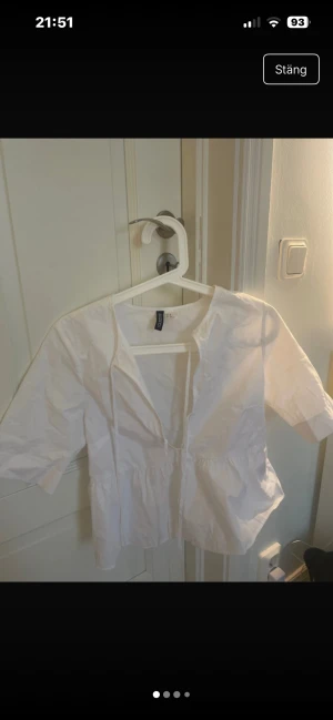 Vit blus med knyt  - Säljer en vit blus med korta ärmar och knytband framtill. Den har en lätt volang nedtill vilket gör den skön och luftig. Perfekt för vår och sommar!