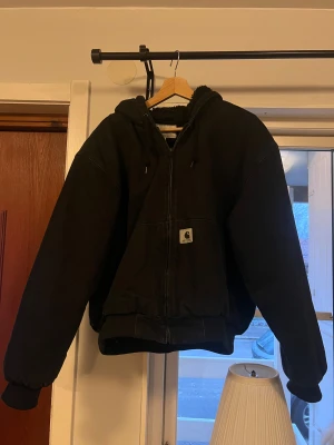Carhartt WIP Active Jacket (Winter edition) - Svart vinterjacka från Carhartt. Detta är den perfekta jackan för någon som vill vara snygg och hålla sig varm på vintern. Jackan ser ut som en jeansjacka/hoodie men den är väldigt bra för vintern. Inuti jackan finns ett pälsfoder som också är innanför huvan. Det finns dun runt händerna som håller armarna varma. Storleken är S men passar även en storlek M bra. Denna jacka köptes för ett år sedan och är i utmärkt skick. Jackan har två små fläckar som är nästan osynliga. 