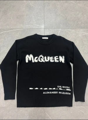 Svart stickad tröja Alexander McQueen - Svart stickad tröja från Alexander McQueen med vit grafisk logotyp på bröstet och detaljerad text vid nederkanten. Rund halsringning och långa ärmar med ribbade muddar. Perfekt för dig som gillar statement-plagg och exklusiva märken. Storlek S passar även M