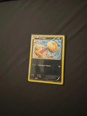 Scraggy (Pokémonkort) - Coolt Pokémonkort med Scraggy, perfekt för samlare och fans! Kortet har färgstark design och visar Scraggy i action med attacken Corkscrew Punch. Ett måste för dig som gillar Pokémon och vill utöka din samling.