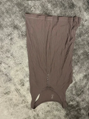 Brun ribbad linnetopp från H&M - Säljer en brun ribbad linnetopp från H&M i storlek L. Toppen har en slim passform, är ärmlös och har snygga knappar framtill. Materialet är mjukt och stretchigt, perfekt för en chill och stilren look. Passar dig som gillar enkla detaljer och neutral färg.