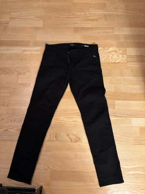 Svarta Replay Anbass jeans herr 32 - Svarta Replay Anbass jeans i klassisk femficksmodell. Slimmad passform med raka ben och snyggt diskret Replay-märke på fickan. Jeansen är tillverkade i ett stretchigt bomullsmaterial som sitter skönt hela dagen.