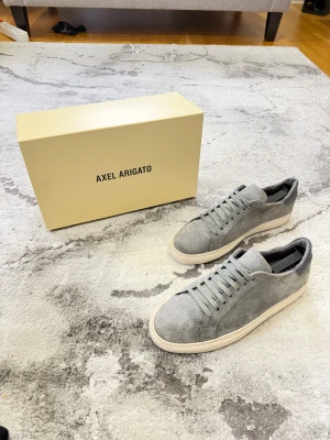 Axel Arigato - Clean 90 Suede - Snygga grå sneakers från Axel Arigato med ovandel i mocka och detaljer i mörkgrått skinn vid hälen. Skorna har rund tå, platt vit sula och klassisk snörning. Perfekt för dig som gillar stilrena och minimalistiska sneakers med premiumkänsla. Köpte från farfetch för 1950kr. Just nu går de för 2650kr retail. Pris går att diskutera!