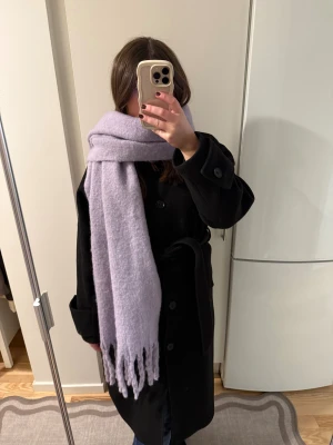 Ljuslila halsduk från STOCKH LM - Supermjuk och fluffig ljuslila halsduk från STOCKH LM, modell Adriana scarf. Halsduken är lång med fransar i ändarna och har en enkel, enfärgad design. Materialet är 82% polyester och 18% ull, vilket gör den både varm och skön att ha runt halsen.