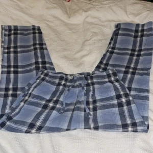 Blårutiga mjukisbyxor med snörning - Blårutiga mjukisbyxor med snörning i midjan. Byxorna har ett klassiskt rakt snitt och är gjorda i mjukt bomullsmaterial. Mönstret är rutig i olika nyanser av blått och svart, vilket ger en chill och avslappnad vibe.Lager157.