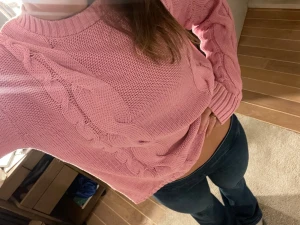 Rosa stickad tröja med flätmönster - Säljer en rosa stickad tröja med flätmönster på både fram- och baksida samt ärmar. Tröjan har rund halsringning, ribbade muddar och lång ärm. Perfekt för dig som gillar en avslappnad och mysig stil med lite extra detaljer.