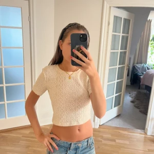 Vit croppad spetsblus med kort ärm - Supersöt vit croppad blus med korta ärmar och rund hals. Toppen har ett detaljerat spetsmönster och är perfekt för dig som gillar en feminin och fräsch stil. Passar till jeans eller kjol och har en lätt loose passform.