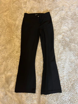 Svarta bootcut kostymbyxor Gina Tricot - Svarta kostymbyxor från Gina Tricot i storlek 34. Byxorna har bootcut-ben, midwaist och klassisk kostymlook med bälteshällor och dragkedja fram. Perfekta för en clean och stilren outfit.