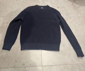 Mörkblå stickad tröja Studio Total - Säljer en mörkblå stickad tröja från Studio Total i storlek M. Tröjan har rund hals, ribbade muddar och är långärmad. Perfekt för dig som gillar enkel och clean stil med lite struktur i materialet.