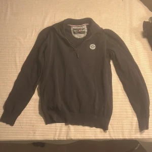 Mörkblå half zip-tröja Polo Club - Snygg mörkblå långärmad tröja från Polo Club Saint Vincent med half zip och ribbad krage. Tröjan har ett broderat märke på bröstet och är gjord i mjuk stickad bomull. Perfekt för dig som gillar klassisk och Grisch stil.