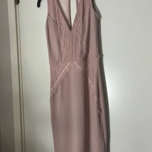 Ljusrosa spetsklänning med v-ringning - Supersnygg ljusrosa klänning med v-ringning och spetsdetaljer framtill och vid midjan. Ärmlös modell med figurnära passform och elegant siluett. Perfekt för dig som vill sticka ut med en romantisk look.