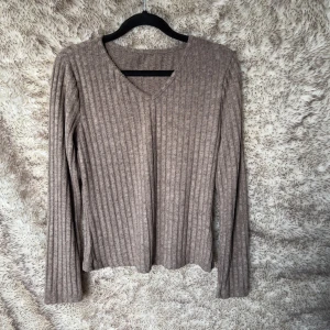 Ribbad beige långärmad tröja - Mysig ribbad tröja i beige med v-ringning och långa ärmar. Tröjan är i ett mjukt och skönt material. 