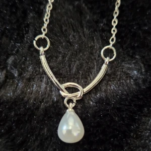 Silverhalsband med droppformad pärla 40+5 cm - Stilrent halsband i silverfärgad metall med tunn kedja och en droppformad vit pärla som hänger i mitten. Kedjan har cirkelformade detaljer och ett elegant, minimalistiskt uttryck. Perfekt för dig som gillar klassiska smycken med en twist.