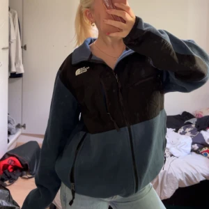 Blå fleecejacka från The North Face - Säljer en blå och svart fleecejacka från The North Face i storlek M. Jackan har dragkedja framtill, hög krage och två sidofickor med dragkedja. Perfekt för lager-på-lager och chill stil. Logga på bröstet och ryggen.