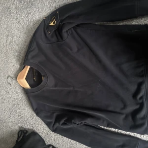 Svart sweatshirt från Moose Knuckles - Svart sweatshirt från Moose Knuckles med rund hals och ribbade muddar. Riktigt fet tröja.