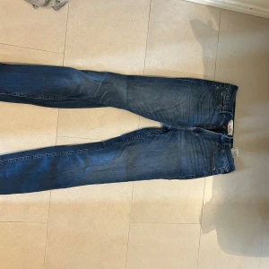 Blå skinny jeans från Hollister W27 L32 - Säljer ett par klassiska blå skinny jeans från Hollister i storlek W27 L32. Jeansen har fem fickor, snygga slitningar och detaljerade bakfickor. Tillverkade i stretchig bomullsdenim för en bekväm passform.