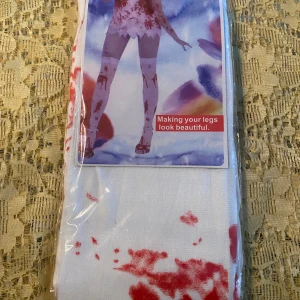 Vita strumpor med röd blodmönster - Unika vita strumpor med rött blodstänksmönster som ger en cool och edgy look. Perfekt för dig som vill sticka ut och ha något annorlunda på benen. Strumporna är tillverkade i mjukt syntetmaterial och passar utmärkt till temafester eller bara för att göra din outfit lite mer intressant. One size 