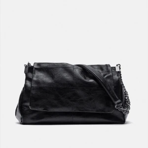 Svart axelväska i skinn med kedja - Snygg svart axelväska i skinn med stilren design och rejäla kedjedetaljer på axelremmen. Väskan har ett stort lock och dragkedja upptill för extra säkerhet. Perfekt storlek för att få plats med allt du behöver och ger en cool vibe till din outfit💕.