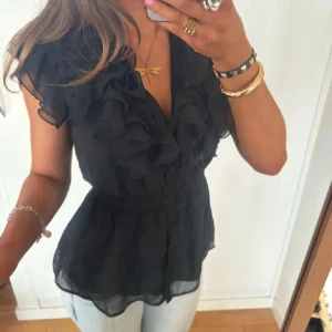 Svart blus med volang - Säljer denna svarta blus med volanger och knappar! Super snygg men lappen med storleken är inte kvar men skulle säga att det är storlek M.💞