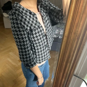 Svartvit rutig trekvarts jacka - Snygg svartvit trekvarts jacka med klassiskt rutigt mönster och stora svarta knappar framtill.  har trekvartsärmar, perfekt att slänga över en t-shirt för en cool look. Materialet känns mjukt och har en stickad känsla.