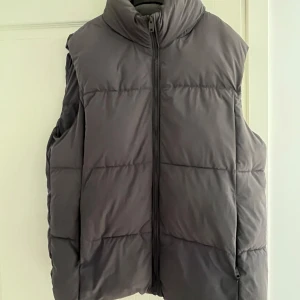Grå mangoväst - Snygg grå dunväst med hög krage och praktisk dragkedja framtill. Västen har en quiltad design och är perfekt för lager-på-lager under kyliga dagar. Enkel och stilren look som funkar till många outfits. storlek M