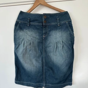 Jeanskjol strl 42 - Denimkjol från H&M storlek 42 i en klassisk blå tvätt. Kjolen har en hög midja med dubbla knappar och fickor framtill. En liten snygg sprunddetalj finns baktill.  Skickas mot porto eller hämtas i Stockholm. 