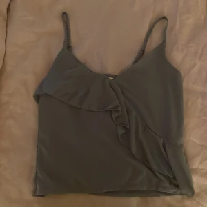 Turkos/grön linnetopp med volangdetalj XS - Säljer en stilren turkos/grön linnetopp i storlek XS med smala axelband och snygg volangdetalj framtill. Toppen har en mjuk och flowy känsla, perfekt att matcha med jeans eller kjol för en trendig look. 🩵