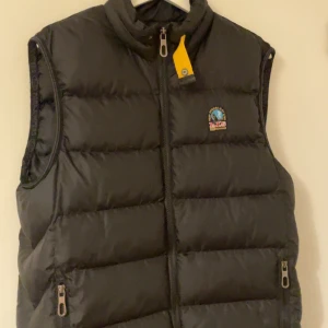 Svart dunväst från Parajumpers - Snygg svart dunväst från Parajumpers med klassisk gul detalj vid kragen och broderad logga på bröstet. Västen har två dragkedjefickor och quiltad design som ger en cool och sportig look. Perfekt för lager-på-lager under höst och vinter.