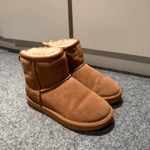 Bruna boots från Sofie Schnoor - Mysiga bruna boots från Sofie Schnoor i mocka med fluffigt foder och platt sula. Perfekta för kalla dagar med sin varma insida och klassiska design. Rund tå och grovt mönstrad yttersula för bra grepp. Sol i nyskick 