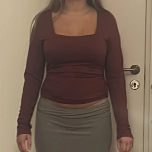 Mörkröd långärmad topp med fyrkantig ringning - Säljer en mörkröd långärmad topp med snygg fyrkantig ringning. Modellen är croppad och sitter tight mot kroppen. Perfekt att styla med både jeans och kjol för en trendig look.