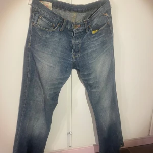 Replay blå jeans med gul detalj - Snygga blå jeans från Jack & Jones med klassisk femficksdesign och gul detalj på fickan. Jeansen har raka ben, kontrastsömmar och cool slitningseffekt. Perfekta för dig som gillar en avslappnad men stilren look.