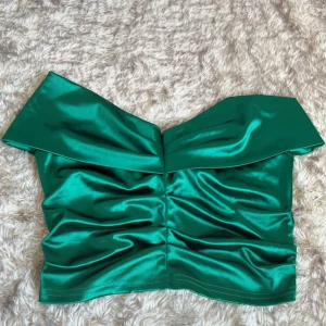 Grön off shouldertopp satin - Fin kort off shounder topp med satin känsla. Rynkor  i mitten och stora band som vilar på axlarna. Stumt material. 