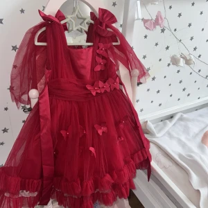 Röd tyllklänning med rosetter och fjärilar - Superfin röd kortklänning i tyll med volanger, stora rosetter på axlarna och 3D-fjärilar med pärlor framtill. Klänningen har puffiga ärmar i transparent tyg och markerad midja. Perfekt för dig som vill sticka ut med en söt och lekfull look.