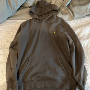 Lyle scott hoodie - Säljer en grön hoodie från Lyle & Scott i storlek L. Tröjan har huva med snörning, känguruficka och den klassiska gula loggan på bröstet. Tillverkad i mjuk bomull, perfekt för chill dagar eller när du vill ha en clean och enkel stil.